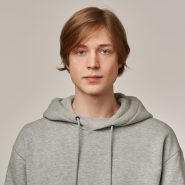 Serious looking male, handsome guy with blond hair. Wearing grey hoodie. People and emotion concept. Watching confident at the camera isolated over grey background Serious looking male, handsome guy with blond hair. Wearing grey hoodie. People and emotion concept. Watching confident at the camera isolated over grey background